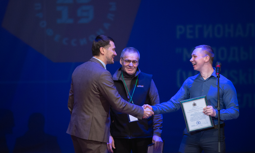 Заместитель председателя правительства Архангельской области по социальным вопросам Артём Вахрушев вручает награду призёру 2018 года и его наставнику.